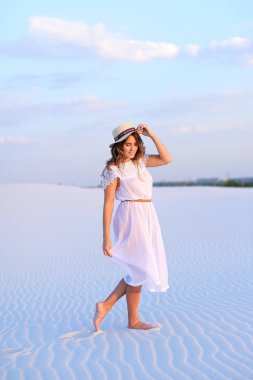 Beyaz elbise ve şapka kumsalda yalınayak gidiş genç kadın.