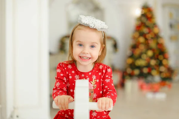 Niña jugando con el caballo mecedora, árbol de Navidad en un fondo borroso . — Foto de Stock