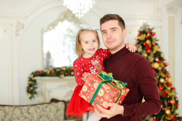 Joven padre feliz manteniendo pequeña hija con regalo, árbol de Navidad en el fondo . — Foto de Stock