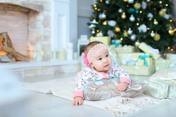 Lilla kvinnliga baby liggande på golvet nära tindrande julgran och julklappar. — Stockfoto