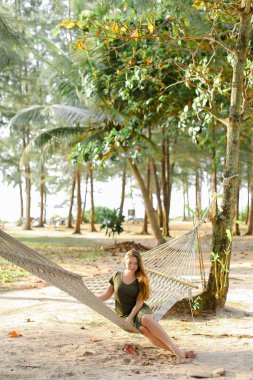 Kum ve avuç içi arka plan ile sepet kamışı hamak oturan yeşil elbise genç güzel kız.