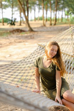 Genç kadın kişi kum ve avuç içi arka plan ile sepet kamışı hamak oturan yeşil elbise güzel. Tropik Adaları ve yaz tatil Tayland seyahat kavramı.