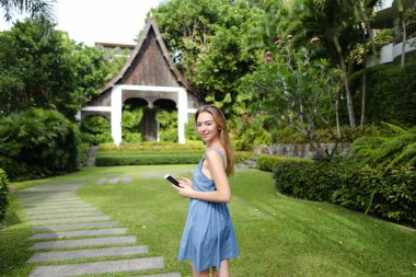 Smartphone kullanarak ve arka plan evde resort ile ayakta sarışın genç kadın.