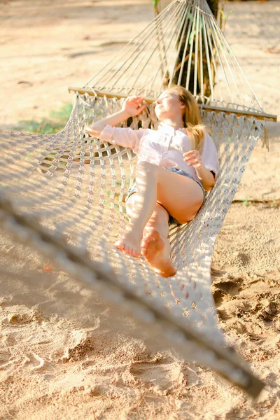 Mujer joven durmiendo en hamaca de mimbre blanca con arena en el fondo . — Foto de Stock