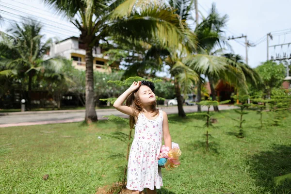 Маленькая белая девочка, стоящая на заднем плане с куклой рядом с пальмами . — стоковое фото