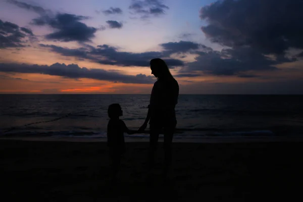 夕日を背景に海の近くの小さな女の子と歩く若い女性のシルエット. — ストック写真