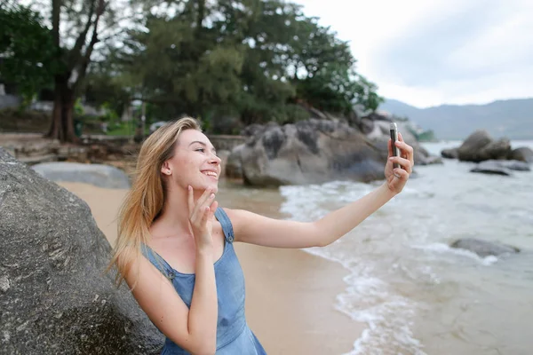 Joven bonita mujer haciendo selfie por teléfono inteligente en la playa vacía cerca del mar . — Foto de Stock