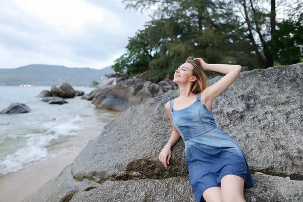 Молодая счастливая женщина, лежащая на камнях на берегу моря утром, в джинсах сарафан . — стоковое фото