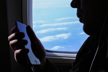 Uçak penceresinde yakınındaki smartphone kullanan adam silüeti portre.