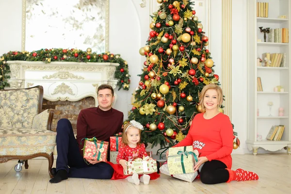 Schwangere blonde Frau sitzt mit Mann und kleiner Tochter neben Weihnachtsbaum und beschenkt. — Stockfoto