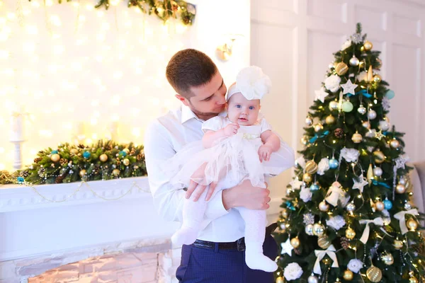 Jovem pai caucasiano mantendo pouco bebê feminino perto da árvore de Natal e lareira decorada . — Fotografia de Stock
