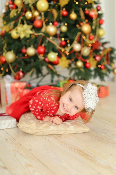 Petite fille femelle couchée sur le sol près de l'arbre de Noël et cadeaux mignons . — Photo
