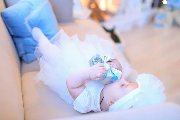 Kleines weibliches Baby liegt auf Sofa und trägt weiße Kleidung. — Stockfoto