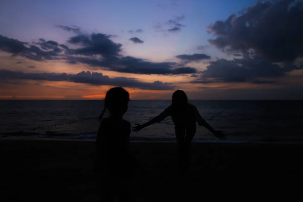 Silhouette nera di giovane donna e ragazza sulla riva del mare al tramonto . — Foto Stock
