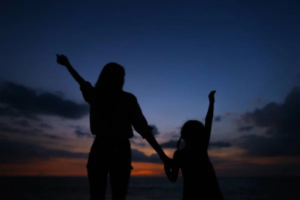 Силуэт женщины и маленькой девочки, идущей в вечернем фоне заката . — стоковое фото