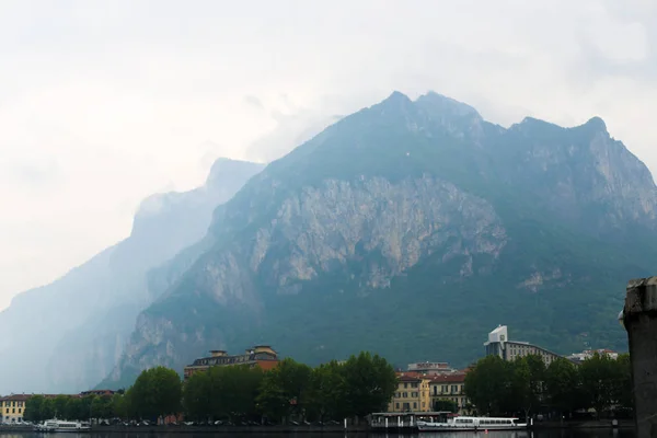 Montagne appenniniche nella nebbia, litorale con edifici e alberi vicino al lago di Como . — Foto Stock