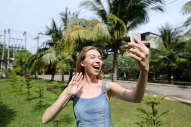 Genç kız smartphone palmiye ağaçları arka planda yakınındaki görüntülü arama yapma.