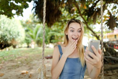 Genç smartphone kullanmasına ve sosyal ağlar, kız salıncak kum üzerinde sürme sevindirmek.