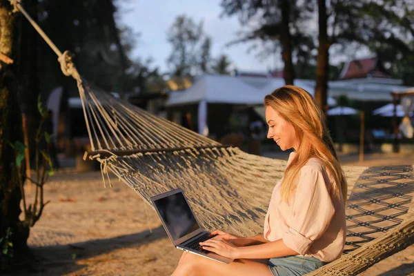 Mujer de negocios que trabaja con el ordenador portátil y sentado en la arena en hamaca de mimbre . — Foto de Stock