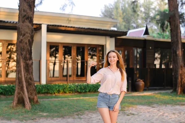 Jonge vrouw staande in de buurt van resort huis en houden van sleutels. — Stockfoto