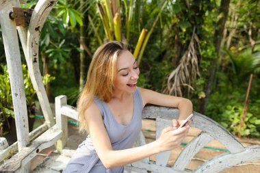 Avuç içinde geçmiş, salıncakta oturan Smartphone kullanan genç kadın.