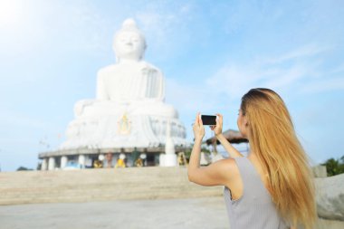 Genç kızın yanında smartphone Buda heykeli Phuket, Tayland için fotoğraf çekici arkadan görünüm.