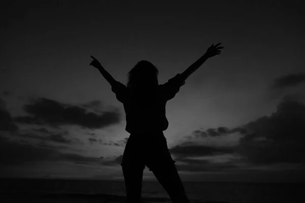 Silhouette nera di persona femminile con le mani alzate sul cielo grigio tramonto a Bali . — Foto Stock