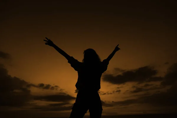 Dark silhouette of girl with raised hands on brown sunset sky with clouds in Bali. — Stock Photo, Image