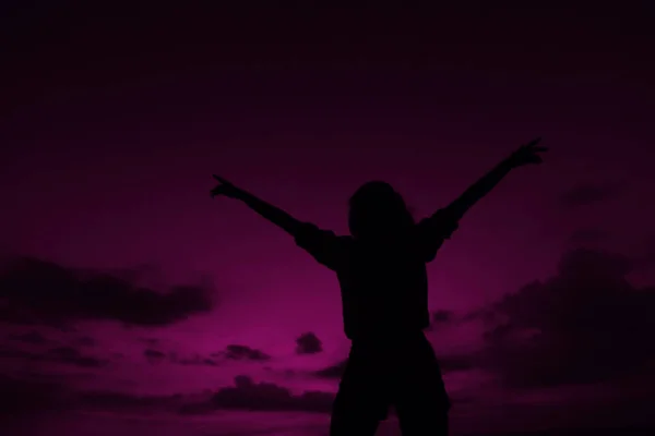 Female black silhouette with raised hands on violet sunset sky background in Hawaii.
