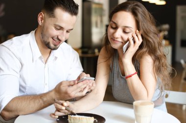 Smartphone ile konuşmak ve kafede bedava bağlantı noktası kullanan adam ile oturan genç güzel kadın.