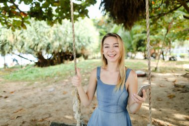 Genç kız salıncak smartphone ile kum üzerinde sürme kot sundress giyiyor.