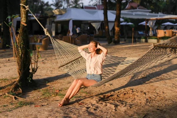 Молодая босиком девушка отдыхает на песке в белом плетеном гамаке . — стоковое фото