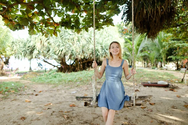 Salıncakta sürme ve kot sundress, arka planda kum giyen genç neşeli kız.