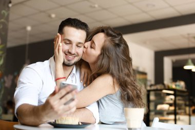 Genç kadın café'de Smartphone kullanarak ve pasta yemeye adam öpüşme.