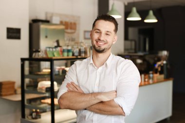 Café'de ayakta ve beyaz gömlek giymiş genç yönetici.