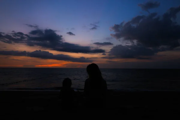 Silhouette di giovane madre che cammina con la piccola figlia vicino al mare al tramonto . — Foto Stock