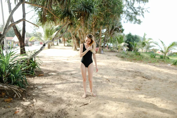 Молодая милая женщина в черном купальнике, стоящая на песке . — стоковое фото