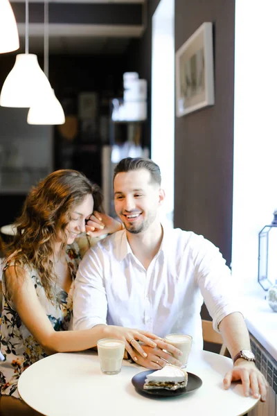 Junges lächelndes Paar sitzt mit Kaffee, Kuchen und Umarmungen im Café. — Stockfoto