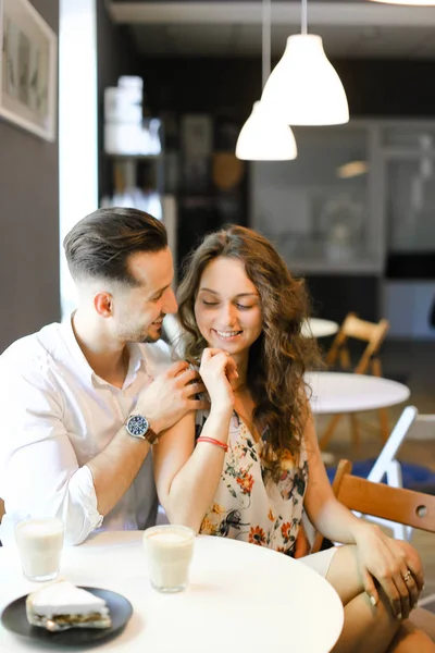 Junger europäischer gutaussehender Herr umarmt Mädchen im Café, sitzt in der Nähe von Tassen Kaffee. — Stockfoto