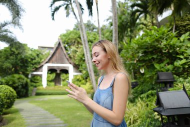 Kot sundress giyen genç Avrupa kadın smartphone Bahçe ağaçları, yakın tarama.