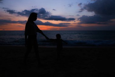 Genç Anne ile küçük kızı deniz kenarında'nde günbatımı yürüme silüeti.
