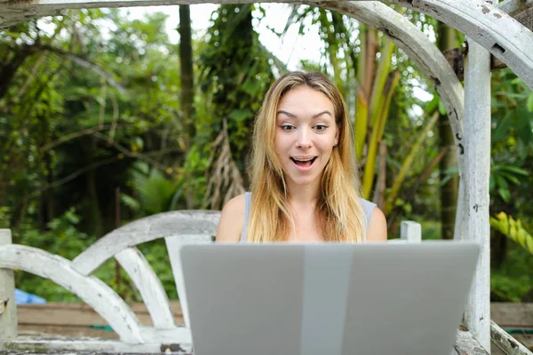 Young woman resting on swing and using laptop, palms in background. — Stock Photo, Image