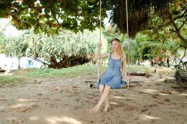 Kot elbise giyiyor ve salıncak, arka planda kum üzerinde sürme Genç beyaz kadın kişi.