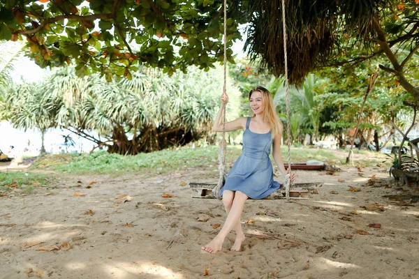 Kot elbise giyiyor ve salıncak, arka planda kum üzerinde sürme Genç beyaz kadın kişi.