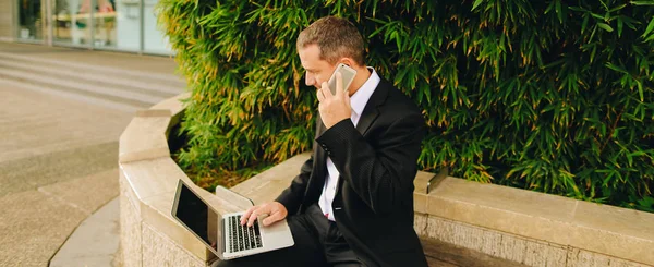 Gerente conversando por smartphone e trabalhando com laptop fora em — Fotografia de Stock