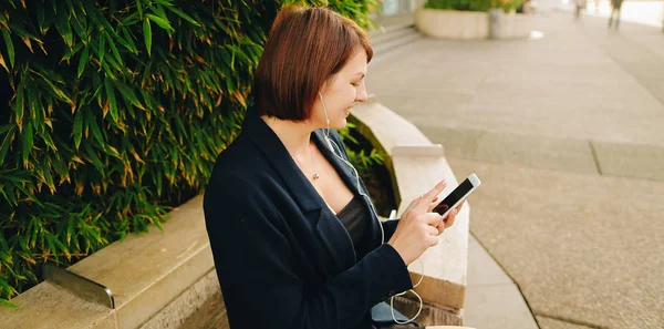 Empresaria escribiendo mensaje y escuchando música afuera con — Foto de Stock