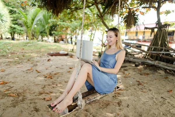Молодая красивая девушка с ноутбуком и катание на качелях на песке . — стоковое фото