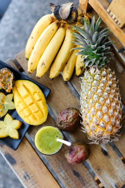 Kiwi fresh green juice near bananas, carambola with mango and pine-apple.