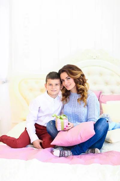 Jovem mãe sentada com filho e presente na cama . — Fotografia de Stock