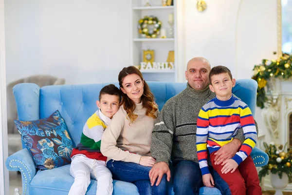 Joven madre y padre sentado en el sofá con los hijos en la habitación decorada para las vacaciones de Navidad . — Foto de Stock